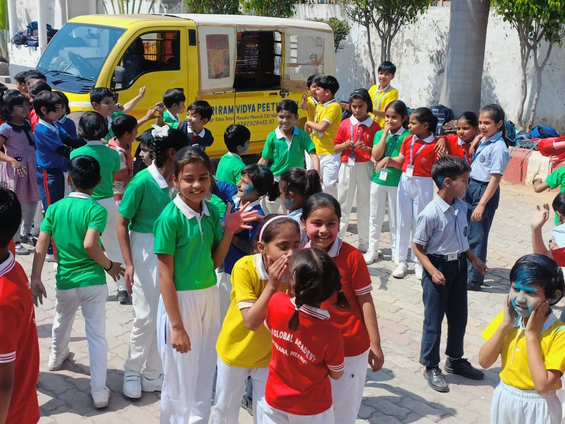 Students celebrating Holi in the school courtyard beside the school buses