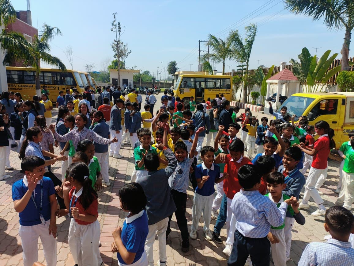 Students celebrating Holi in the school courtyard beside the school buses