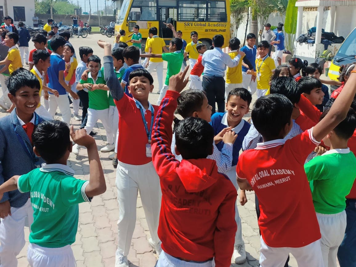 Students celebrating Holi in the school courtyard beside the school buses