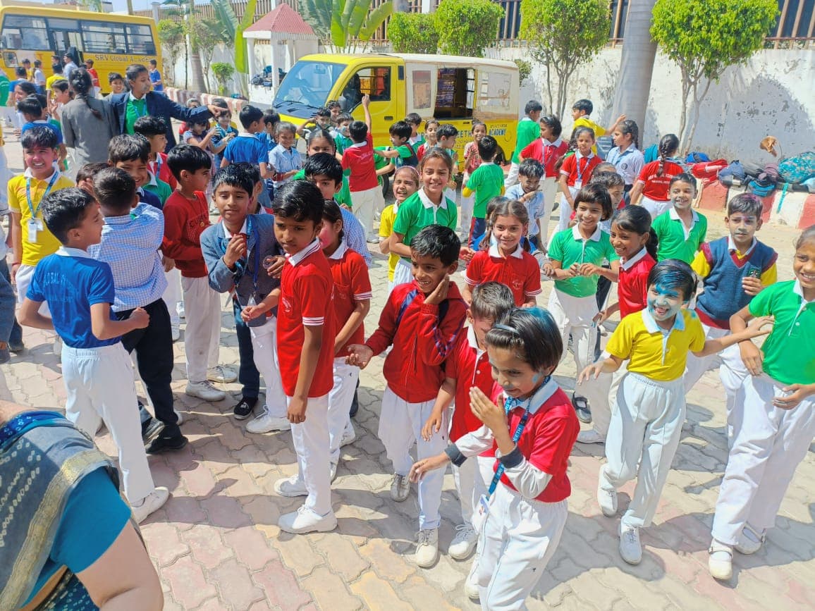 Students celebrating Holi in the school courtyard beside the school buses